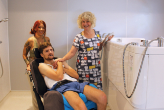 Disabled bather with his carers next to a remote controlled powered raising bath