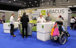 Showing display height adjustable baths to customer in wheelchair at trade show